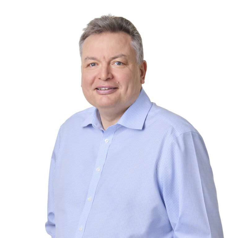 Portrait of a middle-aged man in a light blue checkered shirt, standing against a white background.